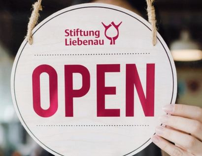 Das Bild zeigt ein Schild mit der Aufschrift "Stiftung Liebenau Open" an einer Glastür