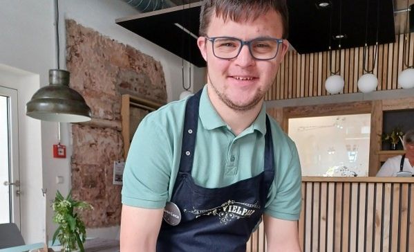 Das Bild zeigt einen jungen Mann mit Schürze in einem Cafe