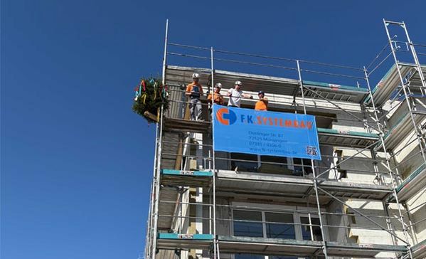Richtfest Ein Gebäude mit einem Gerüst mit Personen darauf.