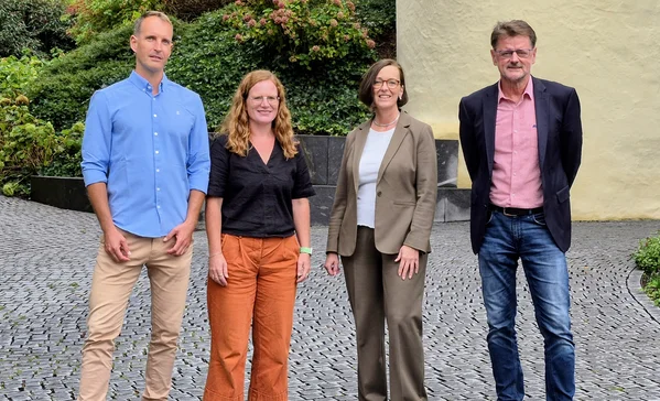 Neue Sozialdezernentin Petra Lill zu Antrittsbesuch in der Stiftung Liebenau Vier Erwachsene — zwei Männer und zwei Frauen — stehen nebeneinander auf einem Kopfsteinpflasterweg vor dem schloss Liebenau, in lässig-formeller Kleidung in die Kamera blickend.