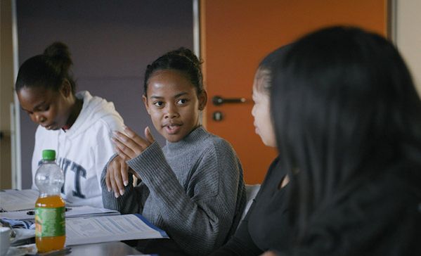 Sprachcafé Mehrere Personen sitzen an einem Tisch und eine Frau spricht.