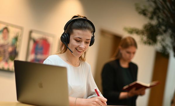 Das Foto zeigt eine Frau mit Headset am Laptop.