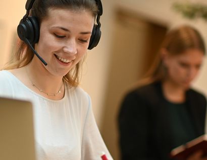 Das Foto zeigt eine Frau mit Headset am Laptop.