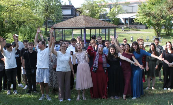 Absolventenfeier Gruppenbild vieler jubelnder Menschen auf einer Wiese.