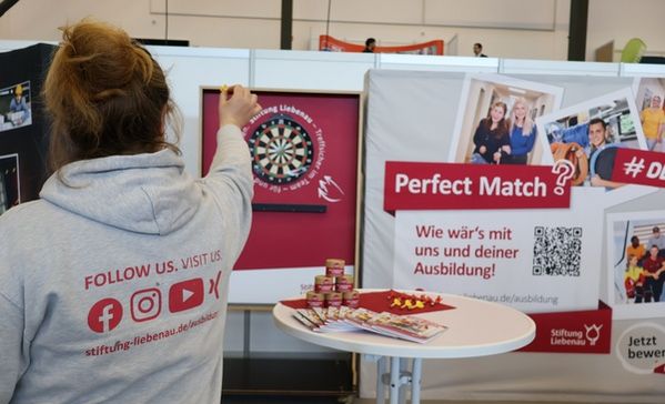 Messen Eine Frau zielt mit einem Dartpfeil auf eine Dartscheibe an einem Messestand.