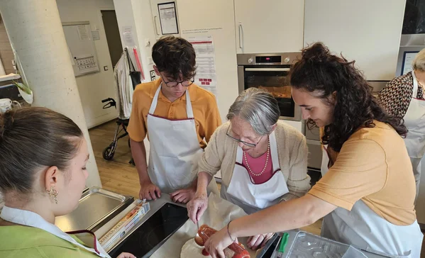 Pizzaaktion im italienischen Flair Vier Personen stehen in der Küche und bestreichen eine Pizza mit Tomatensauce.