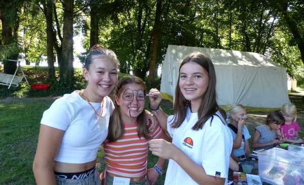 Ferienbetreuung Drei Personen stehen vor einem Zelt und lächeln in die Kamera.