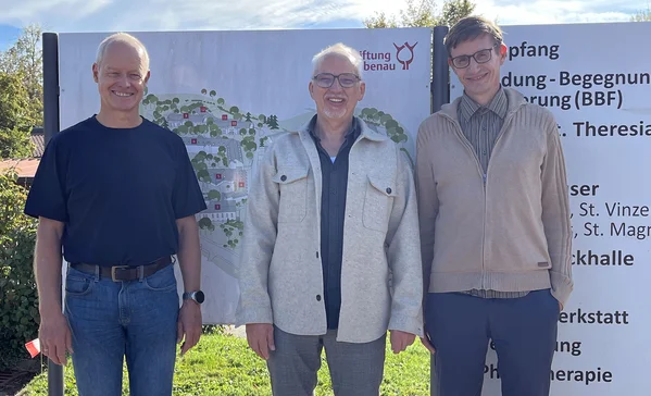 Neues Führungstrio im Fachzentrum Rosenharz Drei lächelnde Männer stehen nebeneinander vor einem großen Informationsschild im Freien, auf einer Grasfläche, in legerer Kleidung.