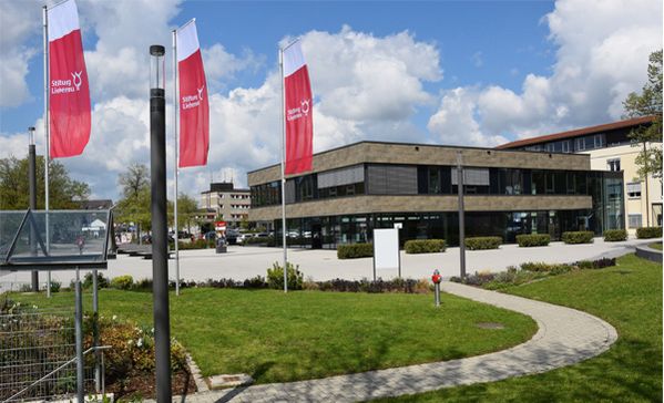 stiftung liebenau weist vorwürfe gegen das gemeindeintegrierte wohnen in markdorf zurück. das foto zeigt den eingangsbereich der stiftung liebenau mit drei fahnen und wiese im vordergrund.