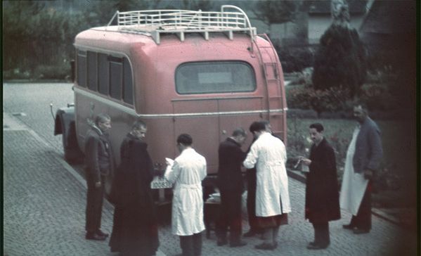 Deportationen Ein altes Foto mit einem roten Bus und Personen davor.
