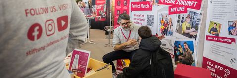 Das Foto zeigt den Messestand. Ein Mitarbeiter erklärt einem Schüler mehr über die Ausbildungsberufe.