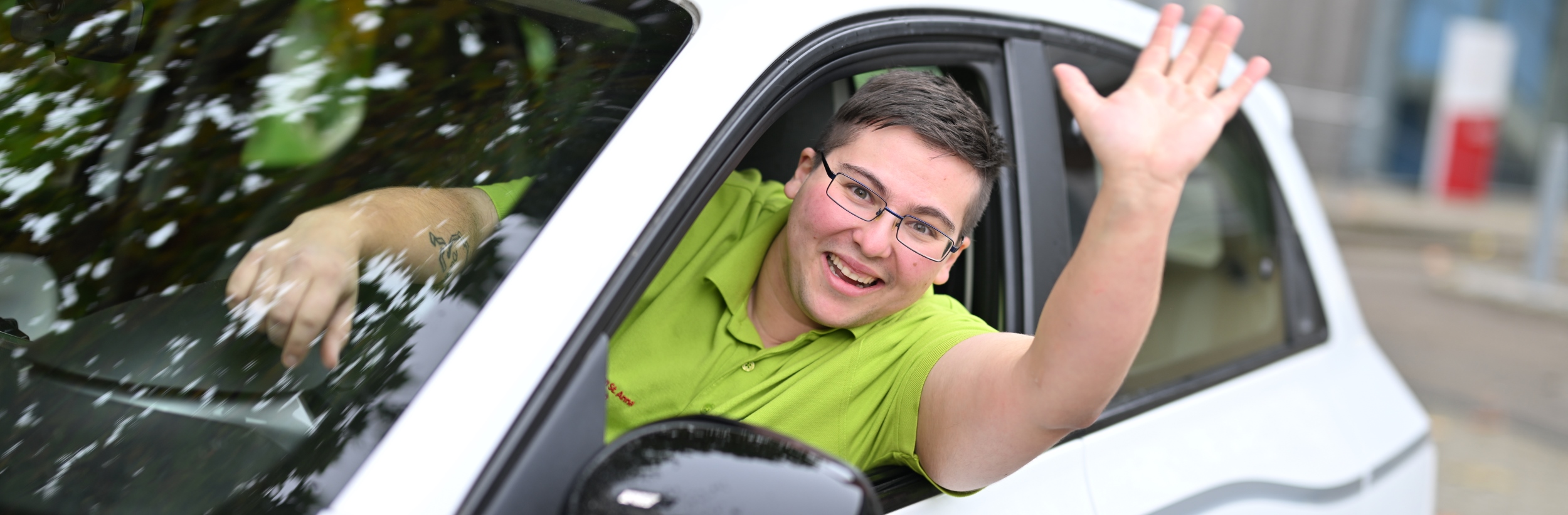 Das Bild zeigt einen winkenden Mann in einem Auto