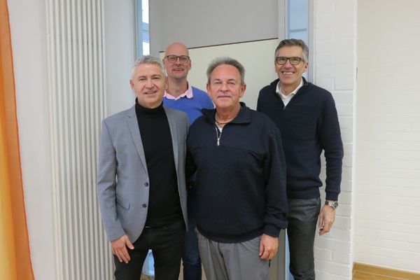 Leitung Das Bild zeigt vier Männer die im Anzug vor der Kamera stehen und lächeln