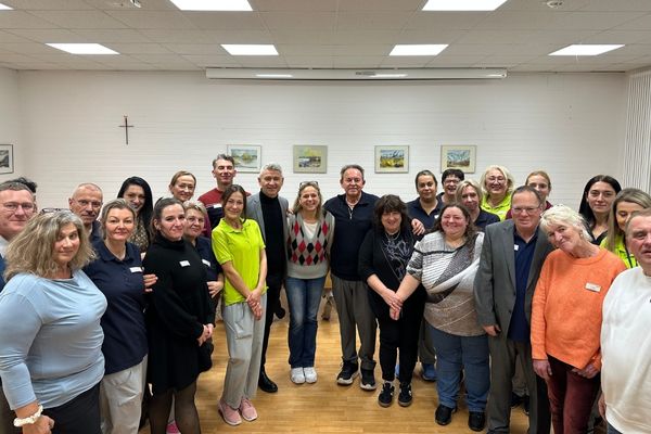 Team Das Bild zeigt eine sehr große Gruppe von Personen die alle gemeinsam in einem Raum stehen und in die Kamera lächeln