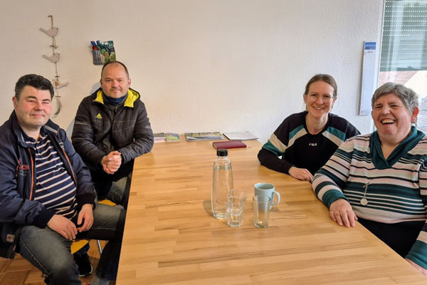 Aktionswoche Vier Personen sitzen an einem Tisch und schauen in die Kamera.