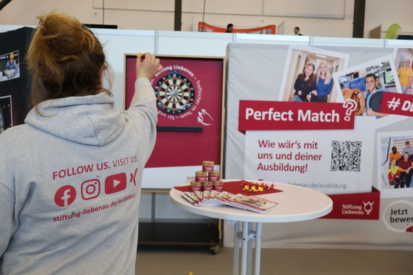 Messen Eine Frau zielt mit einem Dartpfeil auf eine Dartscheibe an einem Messestand.