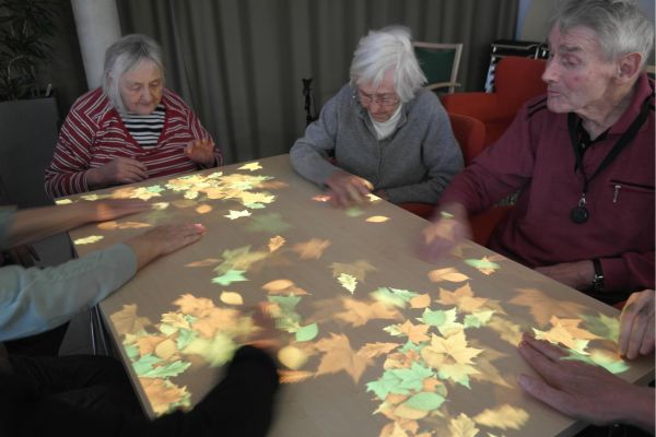 Eine Gruppe älterer Menschen sitzt um einen anprojizierten Tisch