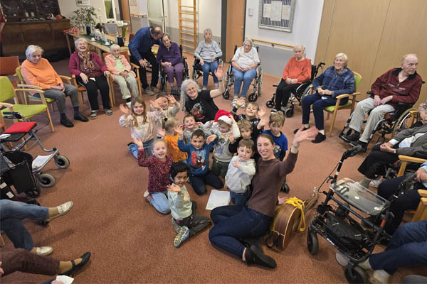 Besuch aus dem Kindergarten Eine Gruppe Kindergartenkinder sitzt in der Mitte eines Stuhlkreises mit vielen Bewohnerinnen und Bewohnern des Pflegeheims.