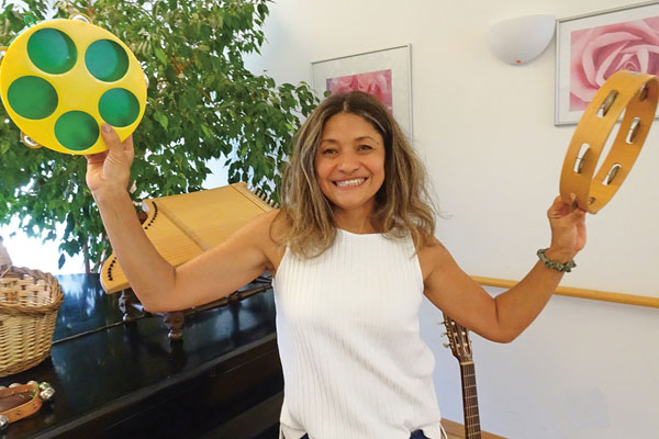 Musik Eine Frau lacht in die Kamera und hält Instrumente in der Hand.