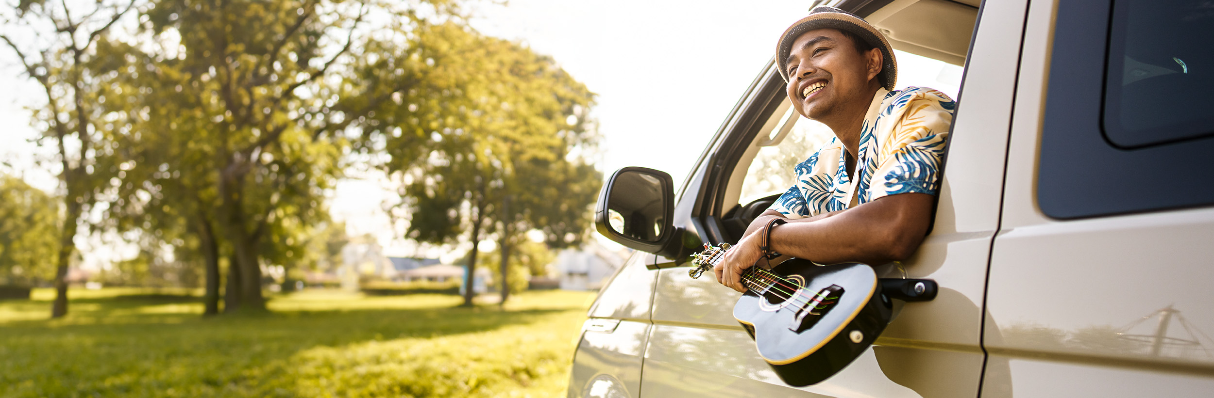 Ein junger Mann, der aus einem Auto schaut und eine Ukulele hält